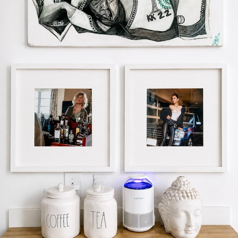 May include: Two white square frames containing photographs, one showing a person at a bar and the other a person by a car. Below are two white ceramic canisters labeled COFFEE and TEA, a white KATCHY insect trap, and a white Buddha head sculpture.