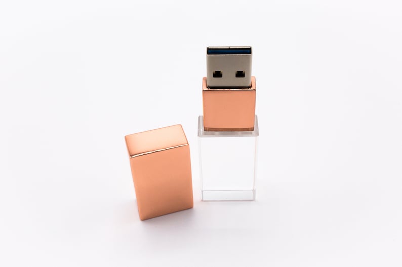 May include: A rose gold USB flash drive with a clear crystal case. The drive is open, revealing the USB connector.