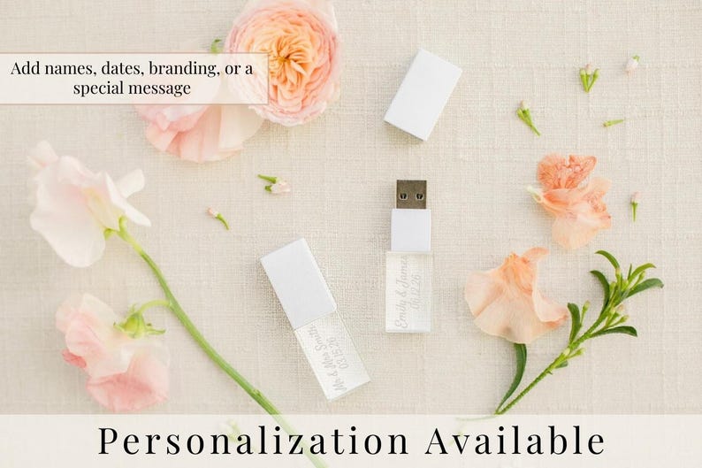 K&ouml;nnte beinhalten: Zwei wei&szlig;e USB-Sticks mit abnehmbaren Kappen und individuell graviertem Text, einschlie&szlig;lich Namen und Daten. Die Sticks sind von pfirsich- und rosafarbenen Blumen umgeben, mit dem sichtbaren Text Add names, dates, branding, or a special message.