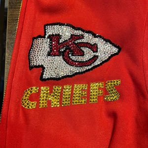 May include: Red sweatshirt with a rhinestone Kansas City Chiefs logo and the word "CHIEFS" in rhinestones.