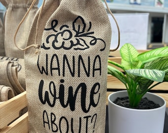 May include: A brown burlap wine bottle bag with a black drawstring and the text "Wanna wine about?" printed on the front.