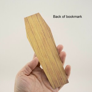 May include: A wooden coffin-shaped bookmark with a wood grain pattern. The back of the bookmark is shown in the image.