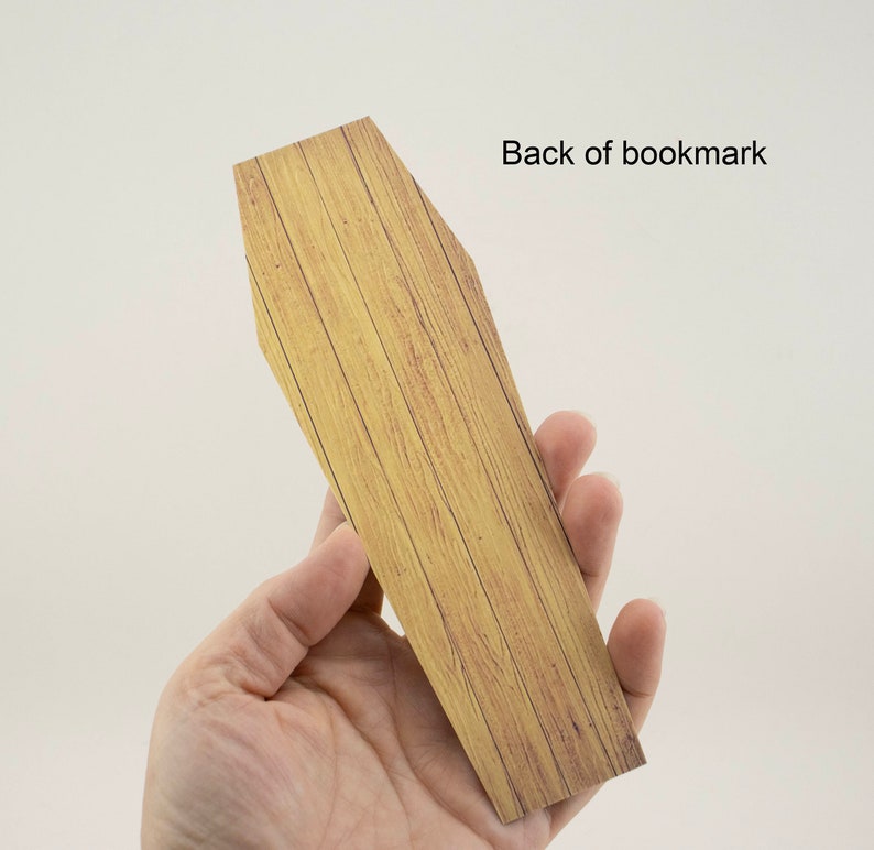 May include: A wooden coffin-shaped bookmark with a wood grain pattern. The back of the bookmark is shown in the image.
