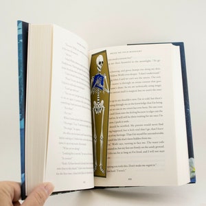 May include: A book open to a page with a skeleton illustration holding a book. The text on the page reads "Bring me your midnight".