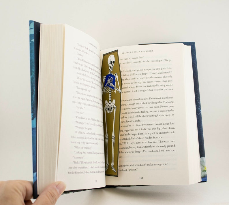 May include: A book open to a page with a skeleton illustration holding a book. The text on the page reads "Bring me your midnight".