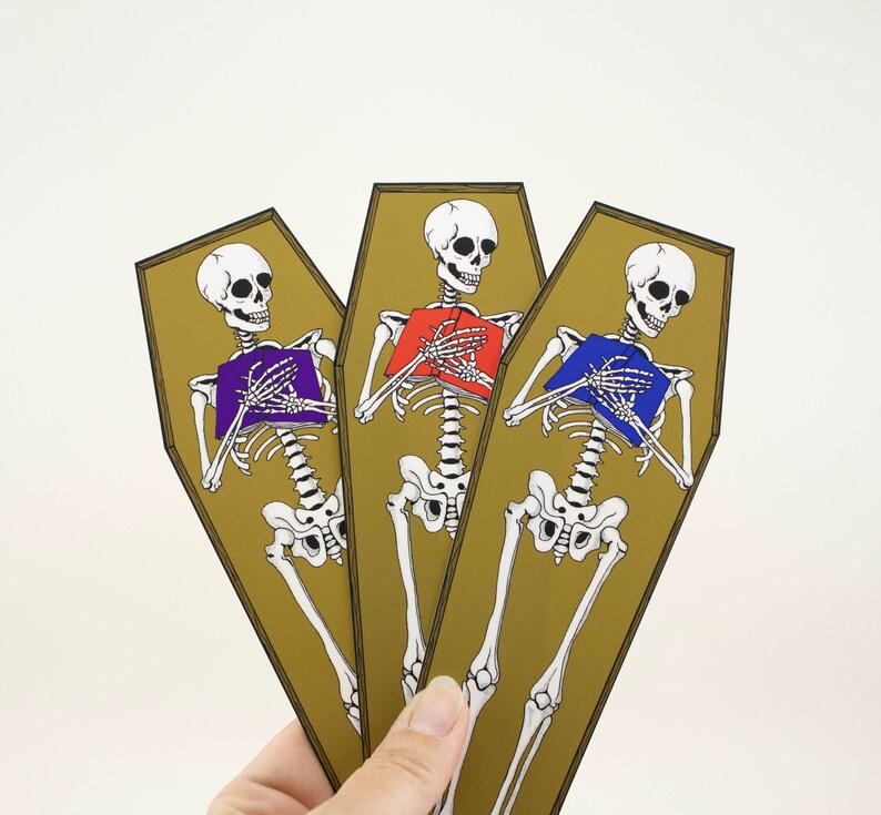 May include: Three gold-coloured coffins with skeletons holding books. The skeletons are wearing purple, red, and blue books. The coffins are standing upright.