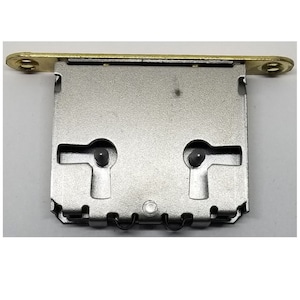 May include: A silver-colored metal lock plate with two keyholes and a brass-colored metal bar at the top.