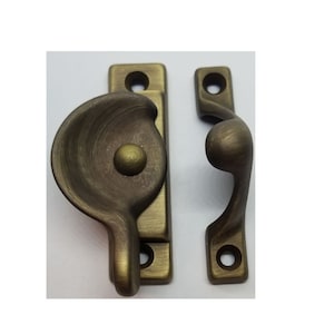 May include: Antique brass window sash lock with a curved handle and a round knob. The lock is designed to secure a window sash in place.