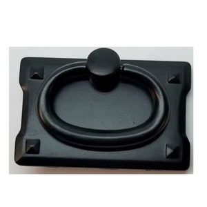 May include: Black metal cabinet pull with a rectangular base and an oval ring handle. The base has four decorative studs.