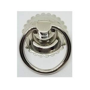 May include: A silver ring pull cabinet knob with a decorative scalloped edge.