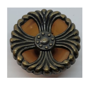 May include: A decorative metal button with a cross-shaped design and a brown center. The button has a detailed, ornate border.