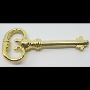 May include: A gold-colored skeleton key with a decorative, ornate head. The key has a long, straight shaft and a simple, flat end.