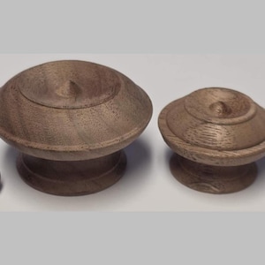 May include: Two wooden cabinet knobs with a dark brown finish, each with a rounded top and a base. Two black screws are also present. The knobs are likely for furniture or decorative purposes.