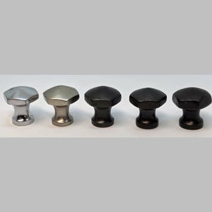 May include: Five cabinet knobs in a row, each with a faceted, hexagonal top. The knobs vary in color, including silver, pewter, and dark bronze. They are designed for furniture or cabinetry.