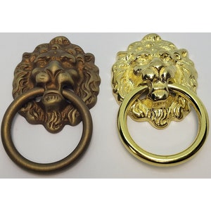May include: Two lion head door pulls, one in antique brass and one in polished brass. Each pull has a ring handle.