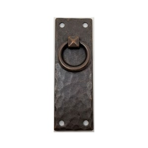 May include: A rustic, hammered metal drawer pull with a ring handle. The pull is dark brown and has two holes for mounting.