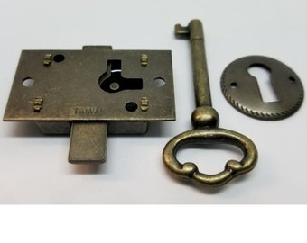 May include: Antique brass keyhole cover, lock, and key. The keyhole cover is round with a decorative edge. The lock is rectangular with a sliding latch. The key has a decorative handle.