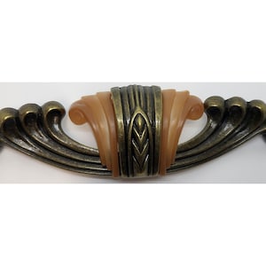 May include: A decorative cabinet pull with a bronze finish and a beige center. The center features a leaf design.