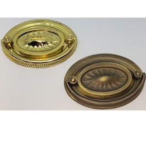 May include: Two oval-shaped cabinet knobs with a decorative design. The knob on the left is polished brass, while the knob on the right is a more antique brass finish.