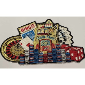May include: A colorful embroidered patch featuring a variety of casino-themed imagery, including a slot machine, roulette wheel, playing cards, dice, and poker chips. The slot machine is labeled "Strike It Rich Silver Dollar".