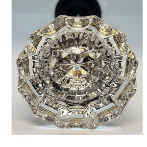 May include: A clear glass door knob with a faceted design and a gold trim. The knob is shown from the bottom, revealing the intricate details of the glass.