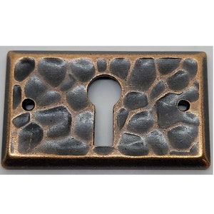 May include: A rectangular keyhole cover with a hammered metal finish. The cover is a dark gray color with a copper-colored border.