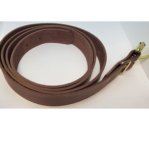 May include: A brown leather belt with a brass buckle. The belt is rolled up and the buckle is visible.