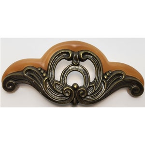 May include: A decorative metal cabinet pull with a brown center and ornate scrollwork design.