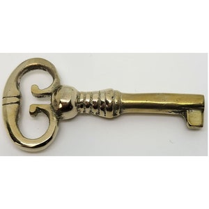 May include: A brass key with a decorative, ornate head and a straight, cylindrical shaft.
