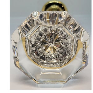 May include: A clear, faceted crystal door knob with a gold-colored base and stem. The knob has an octagonal shape with intricate interior detailing, reflecting light. The stem is a rounded shape.