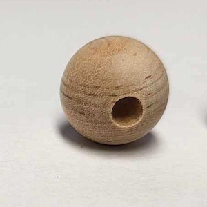 May include: Four spherical wooden beads with holes. The beads are light brown and appear to be made of natural wood. The holes vary in size and placement, with some beads having a hole through the center and others with a hole on the side.