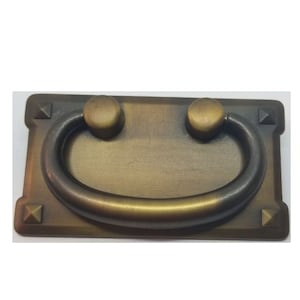 May include: A rectangular, antique brass cabinet pull with a rounded, D-shaped handle. The pull has a textured surface and decorative accents on the corners.