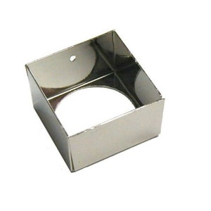 May include: A silver square cake pan with a round hole in the center. The pan is made of metal and has a shiny finish.