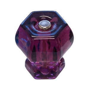 May include: A faceted, purple glass cabinet knob with a silver-colored metal insert. The knob has a hexagonal shape and is designed for furniture. The glass has a deep, rich color and a glossy finish.