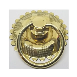 May include: A gold-toned door pull with a decorative, scalloped edge and a ring handle. The pull has a starburst design in the center.