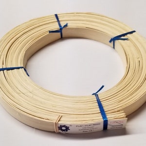 May include: A roll of flat, natural reed for weaving or crafting. The reed is bundled and tied with blue string. The label reads "FLAT/FLAT REED 1/2" WIDE SUPERIOR QUALITY Size: 1/2" x 36"