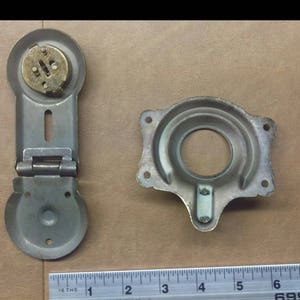 May include: A set of three antique metal lock parts, including a hinged lock with a brass keyhole, a circular lock plate with a keyhole, and a small key. The lock parts are on a brown surface with a ruler for scale.