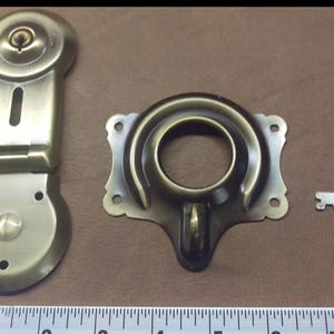 May include: Antique brass latch lock with a key. The lock has a round keyhole and a hinged latch. The key is silver and has a simple design.