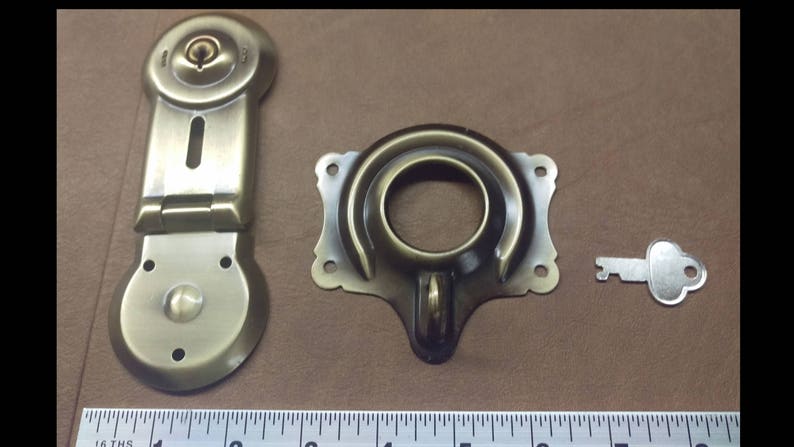 May include: Antique brass latch lock with a key. The lock has a round keyhole and a hinged latch. The key is silver and has a simple design.