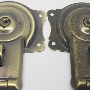 May include: Two antique-style brass cabinet door latches with a keyhole and a hook. The latches have a distressed finish.