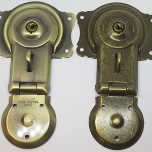 May include: Two antique brass travel bag clasps with a hinged design. Each clasp has a keyhole, a small loop, and a round base with the text "OHIO TRAVEL BAG MADE IN CHINA".