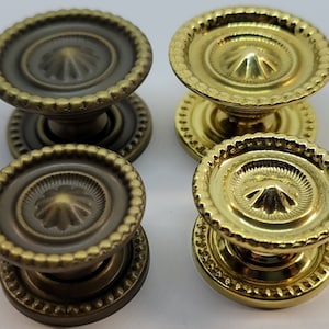 May include: Four decorative cabinet knobs, two in a brass finish and two in a dark bronze finish. Each knob has a raised, circular design in the center and a beaded edge.