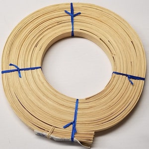 May include: A roll of natural-colored, flat, woven cane, tied with blue ribbon. The cane is used for crafting and weaving.