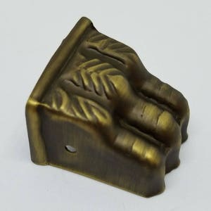 May include: A brass furniture leg with a decorative paw design. The leg is angled and has a hole for mounting.