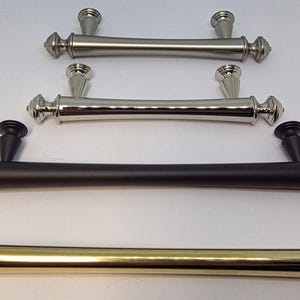 May include: Four metal cabinet pulls arranged in a vertical row, featuring a cylindrical bar design with tapered mounting posts and decorative finials. The finishes include brushed nickel, polished chrome, matte black, and polished brass.