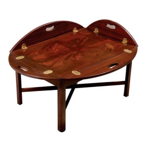 May include: A mahogany-colored, oval-shaped coffee table with a unique design. The table features a folding top with brass hinges and handles. The table is supported by four legs and a connecting support beam.
