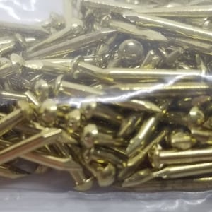 Może przedstawiać: Duża ilość złotych gwoździ tapicerskich lub pinezek w przezroczystym plastikowym opakowaniu.