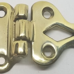 May include: Brass hinge with a decorative design and four holes for mounting. The hinge is closed and has a polished finish.
