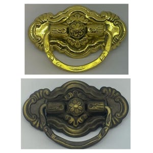 May include: Two ornate cabinet pulls with a decorative floral design. The pull on the top is gold, and the pull on the bottom is a darker bronze color.