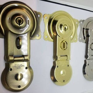 May include: Three antique-style metal clasps with keyholes and decorative details. The clasps are in gold, brass, and silver finishes. The clasps are labeled "Ohio Travel Bag Made in USA".